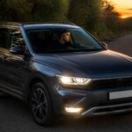 Ciemny SUV z włączonymi światłami na drodze w lesie o zachodzie słońca