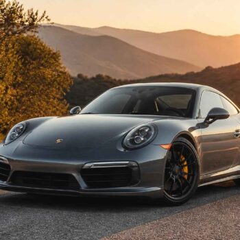 Srebrne Porsche 911 zaparkowane na górskiej drodze o zachodzie słońca