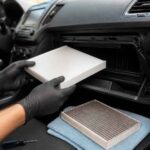 Mechanik w rękawiczkach wyjmuje filtr kabinowy z deski rozdzielczej samochodu
